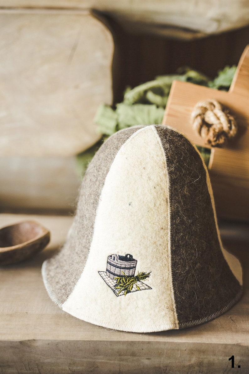 Puede incluir: Un sombrero de fieltro blanco y marr&oacute;n con un dise&ntilde;o bordado de un cubo y trigo en la parte delantera. El sombrero es de estilo tradicional con un ala ancha.
