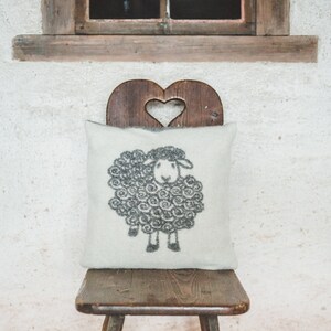 May include: A white pillow with a black sheep design sits on a wooden chair with a heart-shaped cutout in the back.