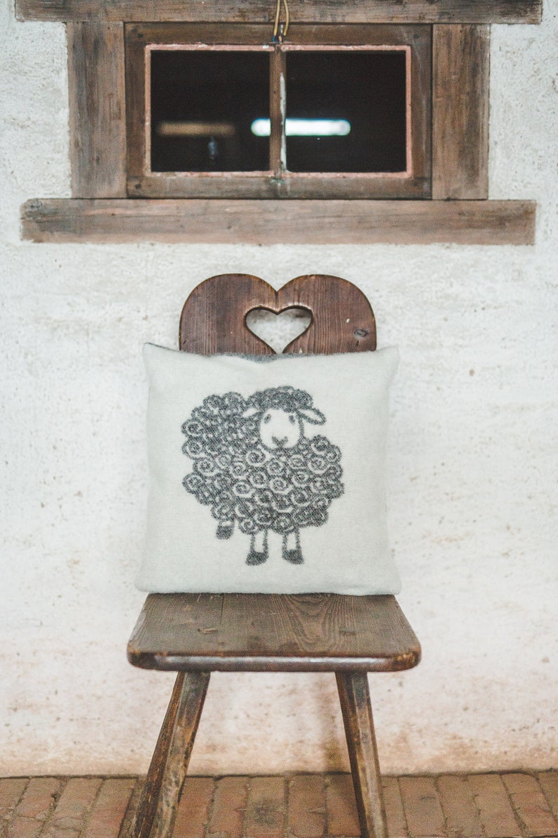 May include: A white pillow with a black sheep design sits on a wooden chair with a heart-shaped cutout in the back.