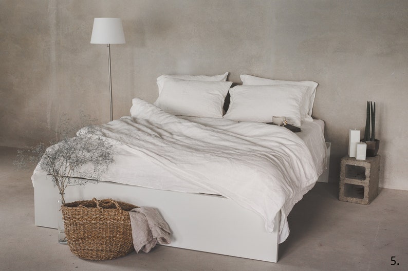 May include: A white linen duvet cover and pillowcases on a white bed frame with a wooden nightstand and a potted plant.