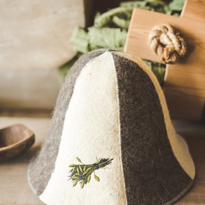 Puede incluir: Un sombrero de fieltro blanco y marr&oacute;n con un dise&ntilde;o bordado verde. El sombrero tiene una corona puntiaguda y un ala ancha.