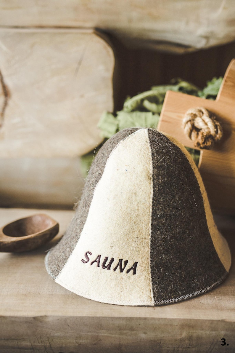 Puede incluir: Un gorro de sauna de fieltro blanco y marr&oacute;n con la palabra "SAUNA" bordada en la parte delantera.