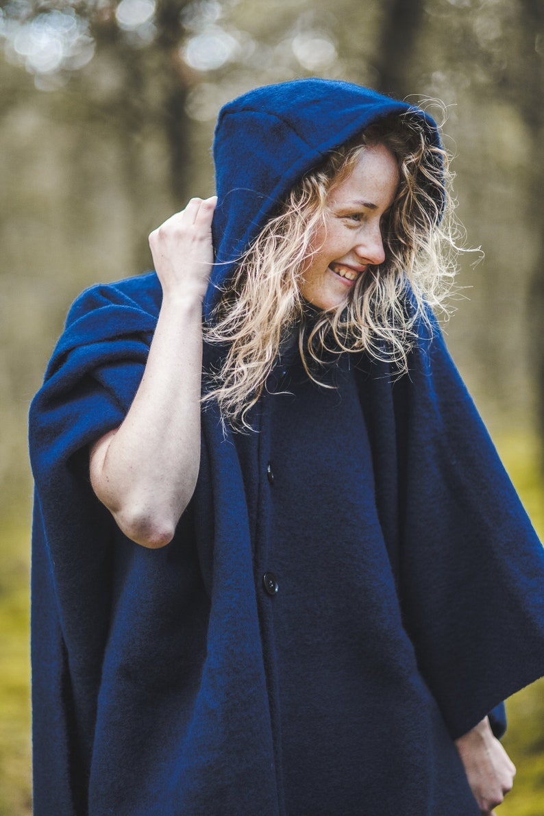 May include: A woman wearing a dark blue hooded cloak with a button closure. The cloak is made of a soft, fuzzy material.