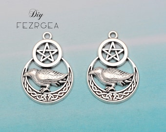 Op de afbeelding: Twee zilverkleurige hangerbedels met een raaf, een wassende maan en een pentagram. De bedels zijn ingewikkeld gedetailleerd en hebben een Keltisch knoopontwerp.