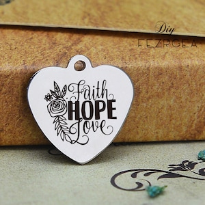 Può includere: Ciondolo a forma di cuore in argento con un design floreale e le parole "Faith Hope Love" incise su di esso.