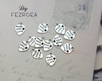 May include: A collection of silver heart-shaped charms with the text "Made with Love" on each charm. The charms have a loop at the top for attaching to jewelry or other crafts.