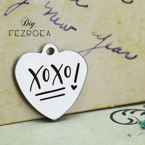 Può includere: Ciondolo a forma di cuore in argento con il testo "XOXO!" in lettere nere. Il ciondolo ha un piccolo anello nella parte superiore per attaccarlo a una collana o un braccialetto.