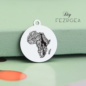 Puede incluir: Un colgante redondo plateado con un gráfico negro detallado del continente africano. La forma del continente está llena de patrones intrincados y una silueta de jirafa. El colgante tiene un pequeño lazo en la parte superior. El texto "DIY FEZRGEA" también es visible.