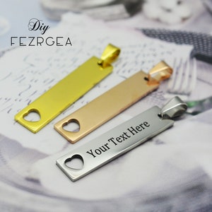 May include: Three rectangular pendants in gold, rose gold, and silver. Each pendant has a heart-shaped cutout and a loop for a chain. The silver pendant has the text "Your Text Here" engraved on it. The pendants are displayed on a patterned surface.