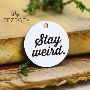 May include: White round charm with a black inscription that reads "Stay weird."