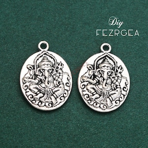 May include: Two oval-shaped, silver-colored pendants featuring a detailed relief of the Hindu deity Ganesha. Each pendant has a loop at the top for attaching to a chain or cord. The pendants are set against a dark green background, with the text "DIY FEZRGEA" visible.