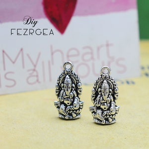 May include: Two silver charms featuring the Hindu deity Ganesha. Each charm is detailed with intricate carvings and has a loop for attaching to jewelry.