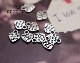 May include: Silver heart-shaped charms with the text "Made with Love" printed on them. The charms have a small loop at the top for attaching to jewelry or other crafts.
