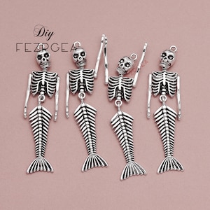 May include: Four silver skeleton mermaid charms with a raised skull and ribcage design. The charms are hanging from a silver loop.