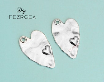Puede incluir: Dos encantos de corazón plateados con un detalle de corazón más pequeño en cada uno. Los encantos tienen una superficie texturizada y un agujero en la parte superior para colgar.