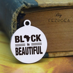 Puede incluir: Un charm redondo de plata con el texto "BLACK is BEAUTIFUL" y una silueta del continente africano.