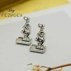 Peut inclure: Deux breloques de microscope en argent, chacune avec un design détaillé et une boucle pour l'attacher à un collier ou un bracelet.