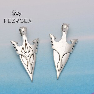 May include: Two silver arrowhead pendants with intricate designs. The arrowheads are pointed and have a three-pronged design at the top.