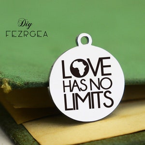 Puede incluir: Un amuleto de plata con el texto "LOVE HAS NO LIMITS" y una silueta negra del continente africano dentro de un círculo.