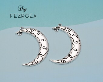 May include: Two silver crescent moon charms with intricate black floral designs. The charms have a loop at the top for attaching to jewelry.