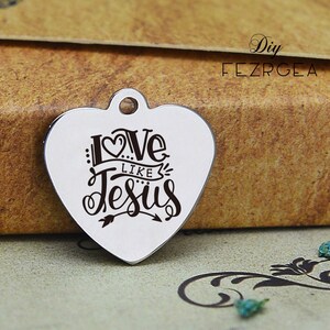 May include: Silver heart-shaped charm with the words "Love Like Jesus" engraved in black lettering. The charm has a small loop at the top for attaching to a necklace or bracelet.
