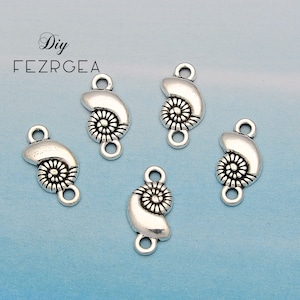 Puede incluir: Cinco dijes plateados con forma de concha marina con un lazo en cada extremo para hacer joyas. Cada dije presenta un diseño en espiral y una forma curva, perfectos para proyectos de bricolaje. Los dijes se muestran sobre un fondo azul claro.