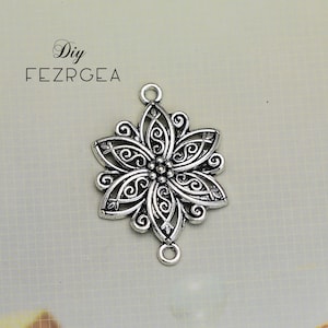 Puede incluir: Encanto de flor de filigrana plateada con dos anillos de salto. El encanto es ornamentado y detallado, con un delicado diseño floral.