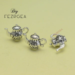 Peut inclure: Trois breloques en forme de théière argentées avec les mots "tea time" gravés dessus.