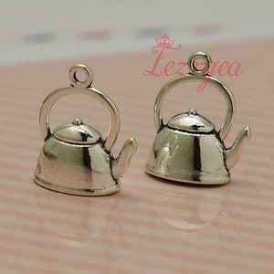 Puede incluir: Dos encantos de tetera de metal plateado con un bucle para sujetar a un collar o pulsera. Los encantos están detallados con un pico, un asa y una tapa.