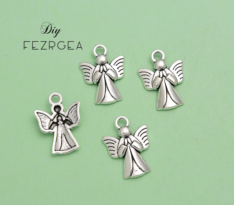 May include: Four silver-colored angel charms with outstretched wings and clasped hands. Each charm has a small loop at the top for attaching to jewelry or other crafts. The background is a light green color.