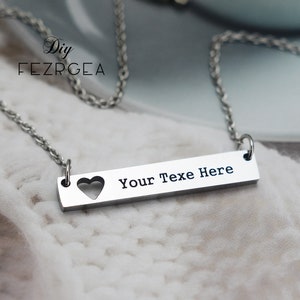 May include: A silver necklace with a bar pendant that says "Your Text Here" with a heart cut out.