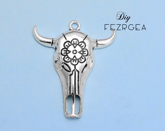 May include: Silver-toned metal bull skull pendant with a decorative floral design on the forehead. The pendant has a loop at the top for attaching to a chain or cord.