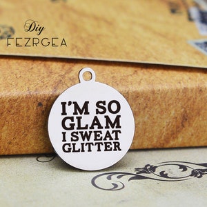 Może przedstawiać: Srebrny charm z napisem "I'm so glam I sweat glitter" w czarnych literach.
