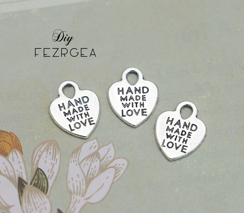 May include: Two silver heart-shaped charms with the text "HAND MADE WITH LOVE" on each charm.