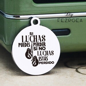 May include: A silver round charm with a black inscription that reads "Si luchas puedes perder si no luchas estas perdido". The charm features two black boxing gloves.