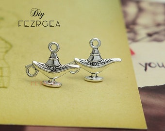 May include: Two silver-toned genie lamp charms with a loop at the top for attaching to jewelry or other crafts.  The charms are detailed with intricate designs and have a vintage look.