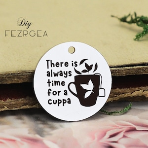 Può includere: Ciondolo rotondo in metallo bianco con una silhouette nera di una tazza da tè e il testo "There is always time for a cuppa".