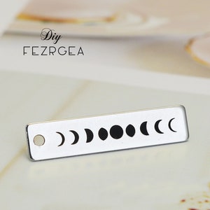 Puede incluir: Un charm de metal plateado con un diseño de las fases de la luna. El charm tiene un agujero en la parte superior para sujetarlo a un collar o pulsera.