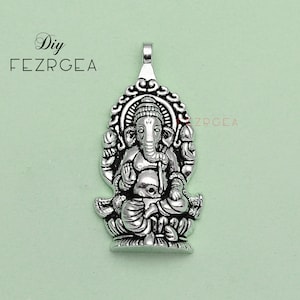 May include: Silver pendant featuring a detailed depiction of the Hindu deity Ganesha, sitting on a lotus throne with his trunk raised and holding a sweet in his hand.