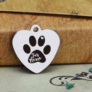 Puede incluir: Una etiqueta de perro de plata en forma de corazón con una huella de pata negra y el texto "Fur Mama" en blanco.