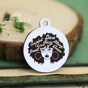 May include: Silver charm with a black and white illustration of a woman with an afro hairstyle. The charm has the words "Diva, Sexy, Strong, Queen, Confident, I Love, Smart" around the woman's head.