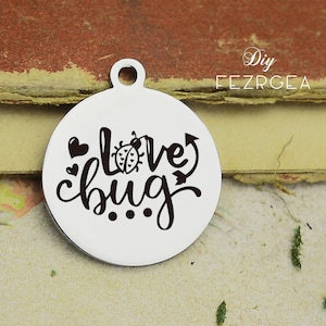 Puede incluir: Un amuleto de plata con una inscripción negra que dice "love bug" con una mariquita y corazones.