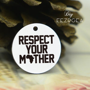 Puede incluir: Encanto redondo de metal blanco con contorno negro y el texto "RESPECT YOUR MOTHER" con una silueta negra del continente africano en el medio de la palabra "MOTHER".
