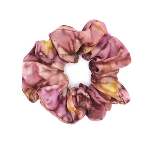 Könnte beinhalten: Ein Haargummi mit einem aquarellartigen Muster in Rosa-, Lila- und Gelbtönen. Der Stoff ist gerafft und elastisch, wodurch ein voluminöses, strukturiertes Accessoire entsteht. Dieses Haargummi eignet sich perfekt, um jeder Frisur einen Farbtupfer zu verleihen.