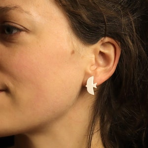 May include: A woman with short brown hair wearing a white bird-shaped earring.