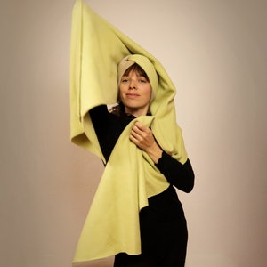 Könnte beinhalten: Eine Frau trägt einen hellgrünen Schal, der über ihren Kopf und ihre Schultern gelegt ist. Der Schal ist aus einem weichen, flauschigen Material. Sie trägt ein schwarzes Oberteil und hat einen neutralen Gesichtsausdruck.