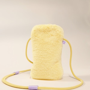 May include: A small yellow fuzzy crossbody bag with a light purple strap. The bag has a small purple tag with the letter "K" on it.