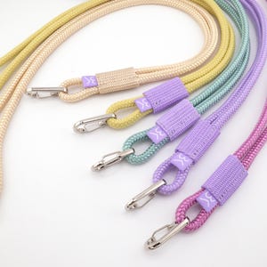 Puede incluir: Una colección de cordones trenzados de colores en tonos beige, amarillo, verde azulado, morado y rosa. Cada cordón tiene un cierre plateado y una banda de tela a juego con un pequeño logotipo. Los cordones están diseñados para llevar objetos.