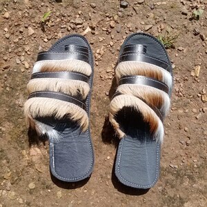 May include: A pair of black leather sandals with brown and white fur trim. The sandals have a simple design and are perfect for casual wear.