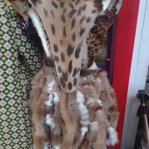 May include: A unique garment featuring a spotted pattern on the upper portion and a fluffy, fur-like skirt. The design incorporates a mix of brown, white, and tan colors, creating a striking visual effect. The garment is displayed on a mannequin.